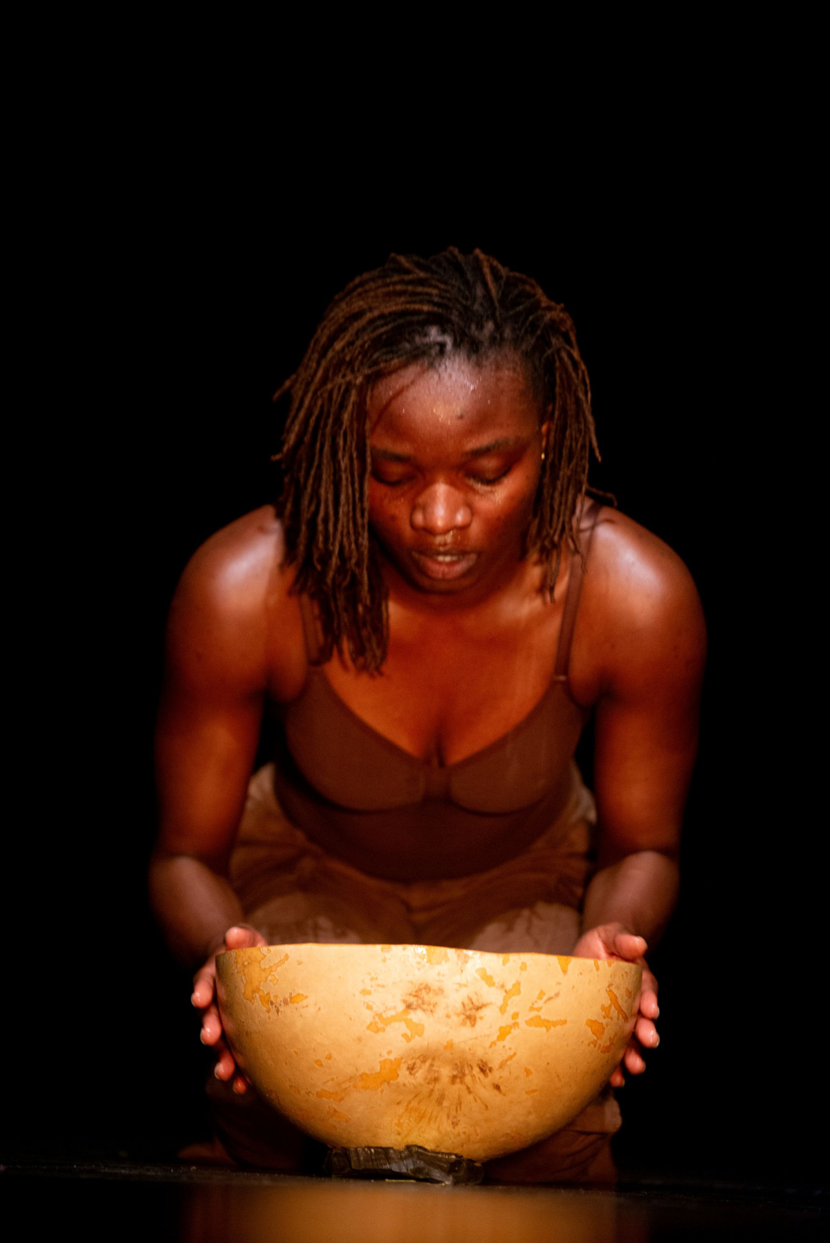 A woman kneeling on the floor is holding up a bowl.