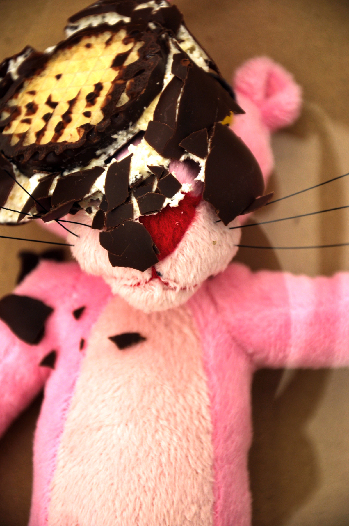 A squashed chocolate marshmallow is lying on the face of a pink panda soft doll.