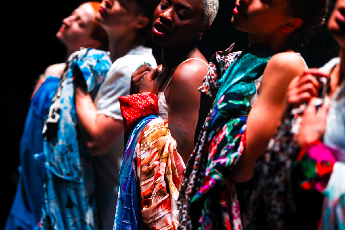Five women are standing in a row, holding colourful items of clothing to their chests.